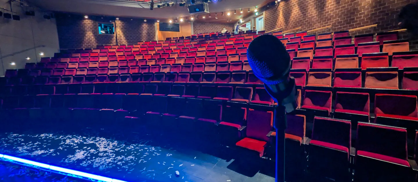 Nach einer Zaubershow liegt Konfetti am Boden. Das Mikrofon für Stand-Up-Zauberkunst steht auf der Bühne wieder bereit.