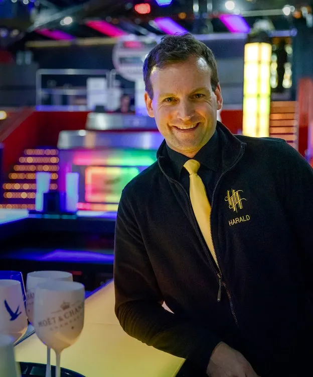 Zauberer Harald Hentschel lehnt sich an eine Bar und ist in einer eleganten Veranstaltungsräumlichkeit zu sehen.